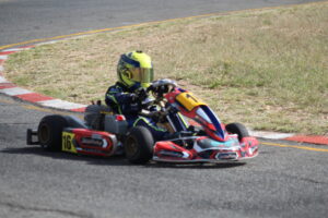 A kart racer in full gear making a tight turn on a racetrack, with focus on the racer's intense concentration and the kart's dynamic angle at Tony Rust Race Track